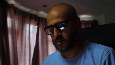 Person-sitting-at-a-desk-wearing-a-blue-shirt,-with-sheer-brown-curtains-and-natural-light-coming-through-the-window-creating-a-warm-ambiance-in-the-background