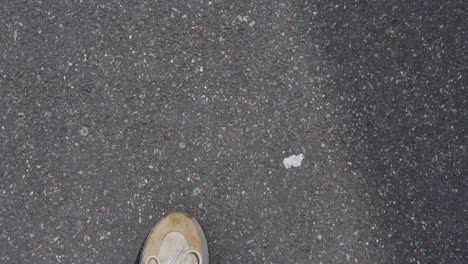 Close-up-of-dirty-trainers-walking-along-worn-asphalt,-showing-rough-pavement-texture