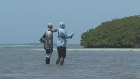 Two-fishermen-wading-in-shallow-tropical-waters-casting-lines-on-a-sunny-day,-side-view