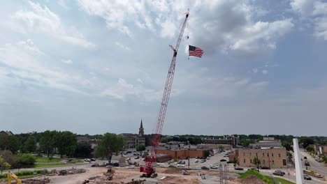 Colgada-De-Una-Grúa-De-Construcción,-La-Bandera-De-Los-Estados-Unidos-Ondea-En-El-Viento.