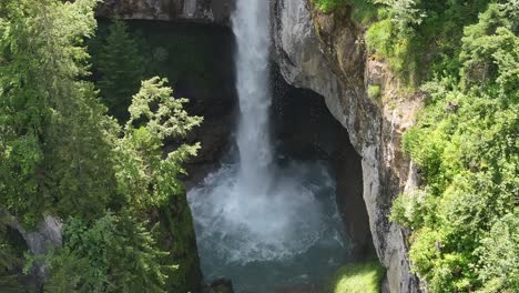 Static-aerial-view-of-water-cascading-down-Berglistüber-Waterfall,-surrounded-by-beautiful-rocks-and-greenery