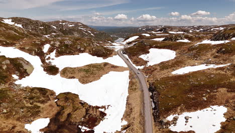 Drone-shot-of-car-driving-in-half-snow-landscape-near-Kjeragbolten-Norway