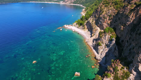 Aerial-ascending-view-of-shallow-sea-and-the-Beach-Calypso,-in-Budva,-Montenegro