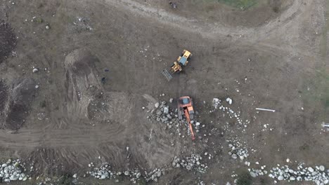 Top-down-aerial-view-of-two-retro-excavators,-one-yellow-and-the-other-orange,-working-on-rocky-terrain