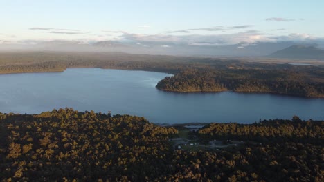 Drone-view-of-lake-Mahinapua-in-between-forests-during-sunset-at-Hokitika,-West-Coast,-New-Zealand