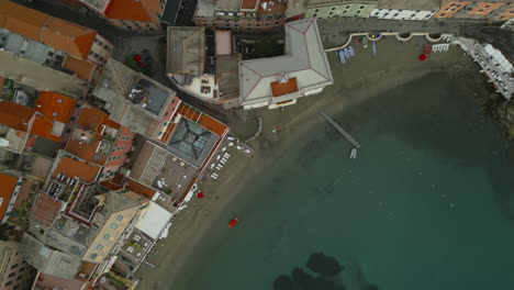 Drone-captures-Sestri-Levante,-Liguria,-Italy,-showcasing-colorful-rooftops,-a-sandy-beach,-and-clear-waters