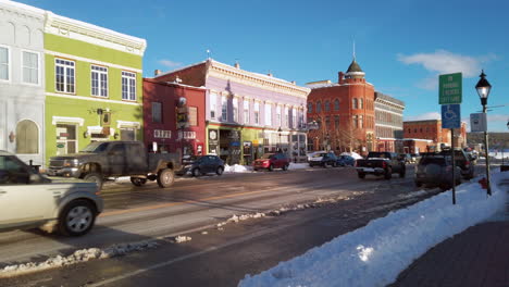 Panning-view-of-downtown-Leadville,-Colorado,-Mainstreet-Harrison-Avenue-with-traffic-on-a-sunny-blue-skay-snowy-day-at-sunset