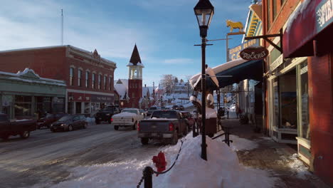 Panning-view-of-downtown-Leadville,-Colorado,-Mainstreet-Harrison-Avenue-with-traffic-on-a-sunny-blue-skay-snowy-day-at-sunset