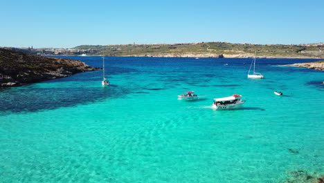 Aerial-drone-shot-flying-backwards-of-boats-riding-along-peacefully-on-crystal-clear,-turquoise-water-on-the-blue-lagoon-at-comino-island-in-malta