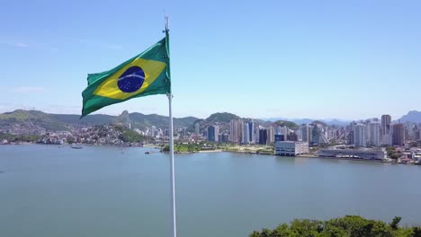 Órbita-De-Drones-De-Bandera-Brasileña-Con-Un-Fondo-Increíble-De-Las-Ciudades-De-Vitória-Y-Vila-Velha,-Hermoso-Día-Soleado-En-Vitória,-Espírito-Santo,-Brasil