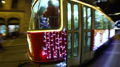 Beleuchtete-Weihnachtsstraßenbahn,-Die-Während-Der-Weihnachtsfeiertage-An-Einem-Platz-Voller-Menschen-Auf-Einer-Belebten-Straße-Vorbeifährt,-Aufgenommen-In-4K-60fps-Zeitlupe