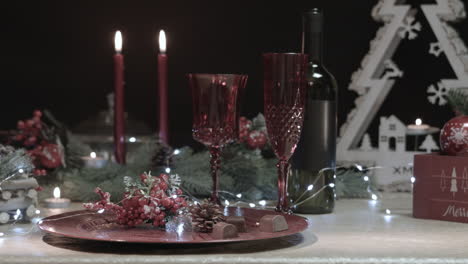 Man-places-a-red-Christmas-tree-ball-on-a-decorated-table-in-a-dark-room,-close-up-shot