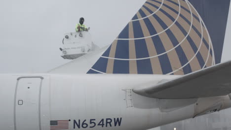 Flight-technician-crew-member-de-icing-tail-of-commercial-aircraft-before-takeoff