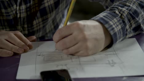 Sketch-artist-drawing-on-sketch-paper-on-top-of-purple-table-with-phone-in-front-of-him