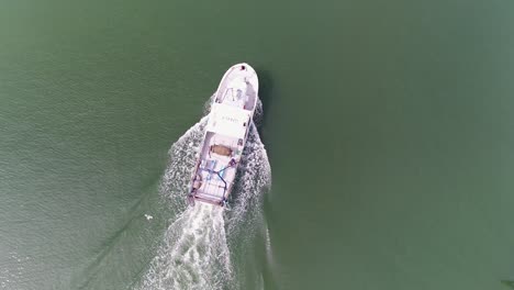 Aerial-view-above-Arenys-de-Mar-fishing-trawler-ship-sailing-out-to-sea-leaving-wave-spray-behind