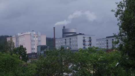 Handaufnahme-Einer-Weitwinkelaufnahme-Von-Norrby-Mit-Wohnungen-Und-Einem-Turm-Im-Hintergrund,-Aus-Dessen-Spitze-Rauch-Aufsteigt-Und-Einem-Wald-Im-Hintergrund