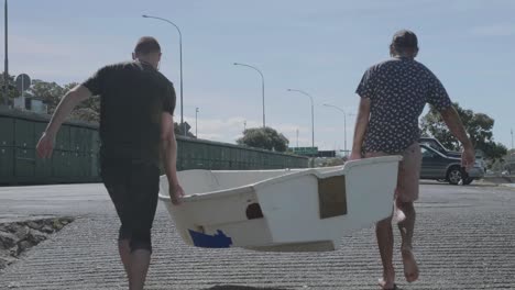 Zwei-Jungen-Tragen-An-Einem-Sommertag-Ein-Altes-Schlauchboot-Eine-Bootsrampe-Hinauf-Zum-Auto-In-Neuseeland