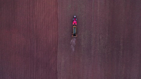 AERIAL:-Descending-Follow-Shot-of-Red-Tractor-Spreading-Manure-on-the-Field-in-Evening,-Manure-Intended-for-Land-Fertilizer-Before-Planting-the-Crop