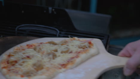 Man-putting-a-homemade-pizza-into-a-wood-fired-pizza-grill-oven-on-a-wooden-plate