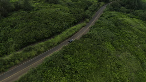 White-vehicle-with-black-top-driving-on-country-road-with-green-foliage,-aerial-shot