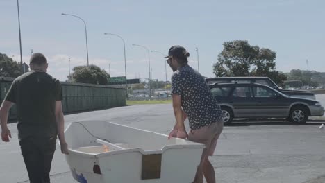 Wide-shot-of-Two-boys-carry-an-old-Dingy-up-a-boat-ramp-to-the-car-in-New-Zealand-on-a-summer-day