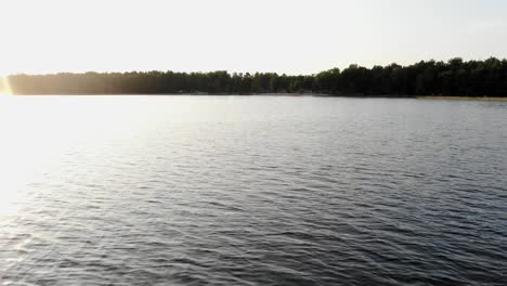 Aerial-dolly-shot-from-a-drone-over-a-lake-with-trees-in-the-horizon