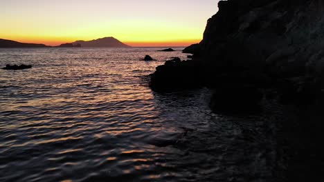 Sunset-or-sunrise-slow-forward-flying-with-colorful-and-dramatic-waves-with-rocky-silhouette-backdrop