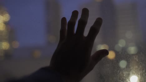 Hand-touching-glass-with-the-city-lights-in-background