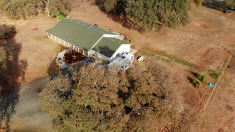 Aerial-Drone-shot-of-a-Rural-Farm-home-a-fly-over-and-pan-up-with-oak-trees-to-blue-sky