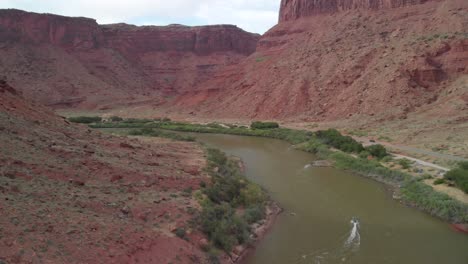 Aerial:-Boat-motors-up-green-Colorado-River-in-towering-red-canyon