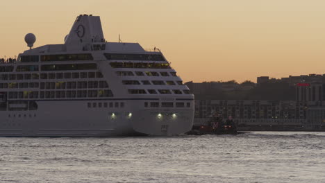 Heckansicht-Eines-Kreuzfahrtschiffs,-Das-Während-Der-Goldenen-Stunde-Von-Einem-Schlepper-Entlang-Des-Hudson-River-Unterstützt-Wird