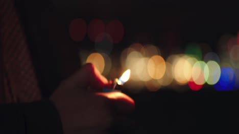 Man-fires-gas-lighter-outdoors-on-windy-night-on-blurred-lights-at-background