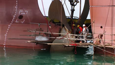 Tilt-up-from-sea-to-oil-tanker-propeller-being-repaired-by-engineers-on-a-scaffolding-surrounding-the-propeller