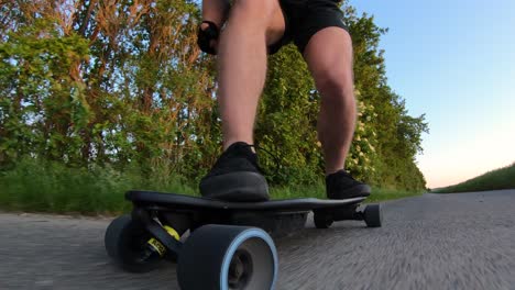 riding-an-electric-longboard-in-black-boots-and-shorts-in-countryside,-low-angle,-close-up,-shaky