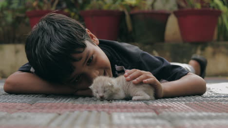 THE-CARING-FRIEND-,-A-young-boy-is-playing-and-caring-a-new-born-kitten-while-lying-on-a-floor