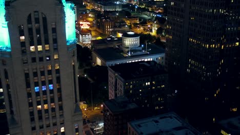 Aerial-view-away-from-the-Ohio-Statehouse-and-the-LeVeque-Tower,-in-Illuminated-Columbus-city---rising,-pull-back,-drone-shot