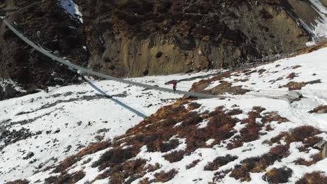 A-solo-trekker-walking-towards-on-a-suspension-bridge-with-frozen-river-bed-below