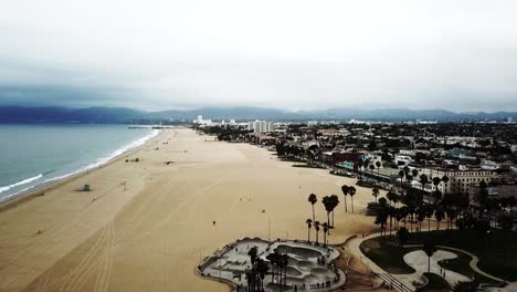 Venice-Beach-Caliornia-on-a-grey-rainy-day,-aerial-drone-shot-flying-north-on-the-shoreline-towards-Santa-Monica