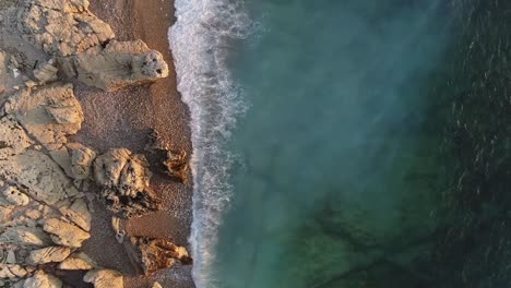 Top-view-shot-of-blue-waves-hitting-the-rocky-shore