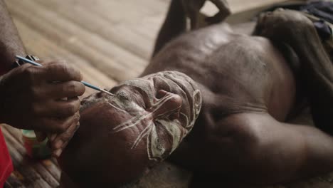 Close-up-shot,-indigenous-man-face-painting-another-man-inside-the-hut