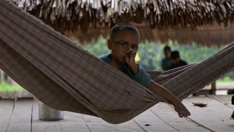 Un-Niño-Tribal-Brasileño-Se-Sienta-En-Una-Hamaca-Y-Mira-La-Cámara-Seriamente