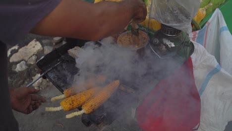 Close-up-shot-of-Corn-on-the-cob-being-brushed-with-seasoning-and-grilled-and-smoked-on-a-food-cart-on-the-streets-of-Bali-Indonesia,-Slow-Motion