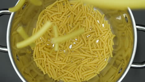 Top-view-in-slow-motion,-macaroni-pasta-falling-into-a-metal-pan-on-a-slate-grey-background