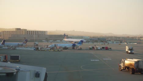 Weite-Aufnahme-Des-Internationalen-Flughafens-Von-San-Francisco,-Während-Flugzeuge-Und-Lastwagen-Mit-San-Francisco-Im-Hintergrund-Rollen