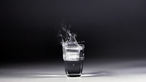 Ice-falls-into-a-transparent-glass,-then-water-splash-out,-all-in-slow-motion