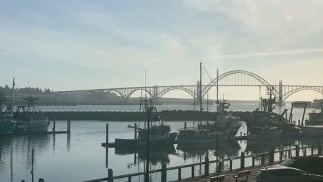 Fishing-Boats-At-The-Harbor-Of-Newport,-Oregon-With-Yaquina-Bay-Bridge-In-Background