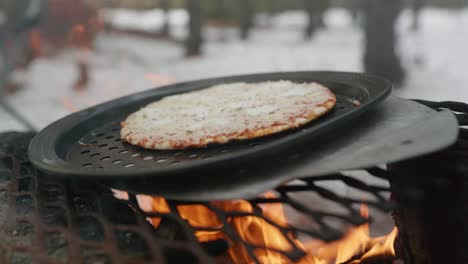 Cheese-pizza-cooking-on-a-steel-grate-over-an-open-fire