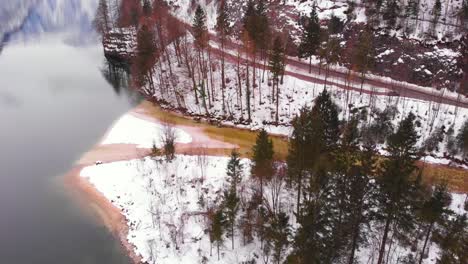 Snowy-shoreline-at-a-quiet-lake-in-Europe-during-cold-winter,-drone-shot-HD