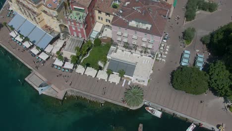 Birds-eye-drone-shot-of-the-promenade-in-the-center-of-Riva-Del-Garda-with-the-garda-lake-and-some-hotels-from-above