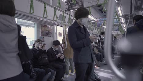 Vista-De-Personas-Con-Máscaras-Usando-Teléfonos-Celulares-Dentro-De-Un-Tren-En-Tokio,-Japón---Plano-Medio